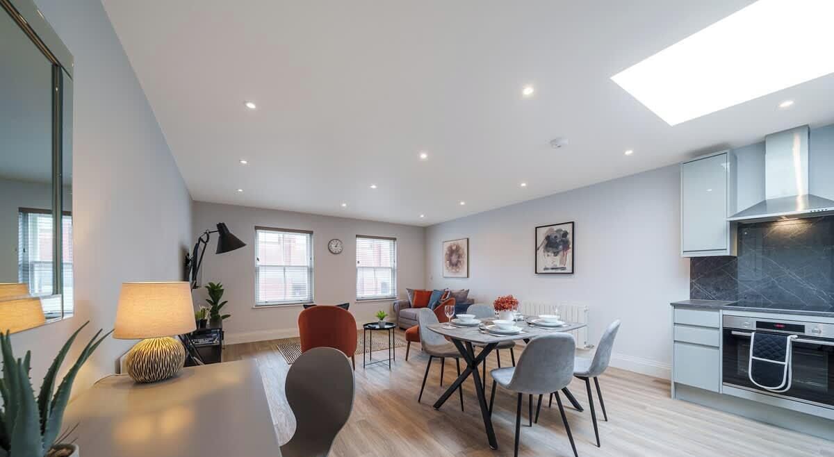 A modern kitchen with a built-in oven, a dining area with a round table and chairs, and a living area with a sofa and a coffee table.