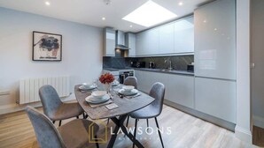 A modern kitchen with grey cabinets, a central island, and a dining area with a table set for four. - Central Windsor Gem | 1BR Penthouse + Balcony (Windsor)