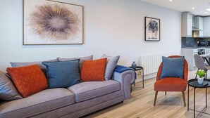 A modern living room with a sofa, armchairs, and a coffee table. There is a kitchen in the background. - Central Windsor Gem | 1BR Penthouse + Balcony (Windsor)