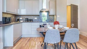 A modern kitchen with white cabinets, a central island, and a dining area with grey chairs. - 3-Bed, 3-Bath Apartment with Southsea Common Views (Portsmouth)