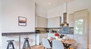 A modern kitchen with a dining area, featuring a marble countertop, stainless steel appliances, and a large window.
