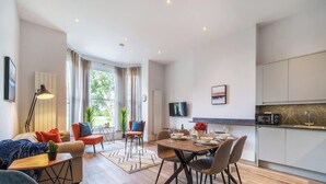 A modern living room with a dining area, kitchen, and large windows. - 3-Bed, 3-Bath Apartment with Southsea Common Views (Portsmouth)