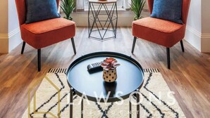 A room with two red chairs, a small table, a clock on the wall, and a view of greenery outside. - 3-Bed, 3-Bath Apartment with Southsea Common Views (Portsmouth)