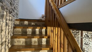 Una escalera de madera con paredes de piedra, barandilla de madera y un cuadro enmarcado en la pared.