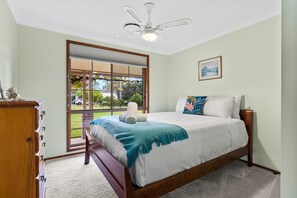 A bedroom with a bed, a wooden dresser, a ceiling fan, a window, and a painting on the wall.