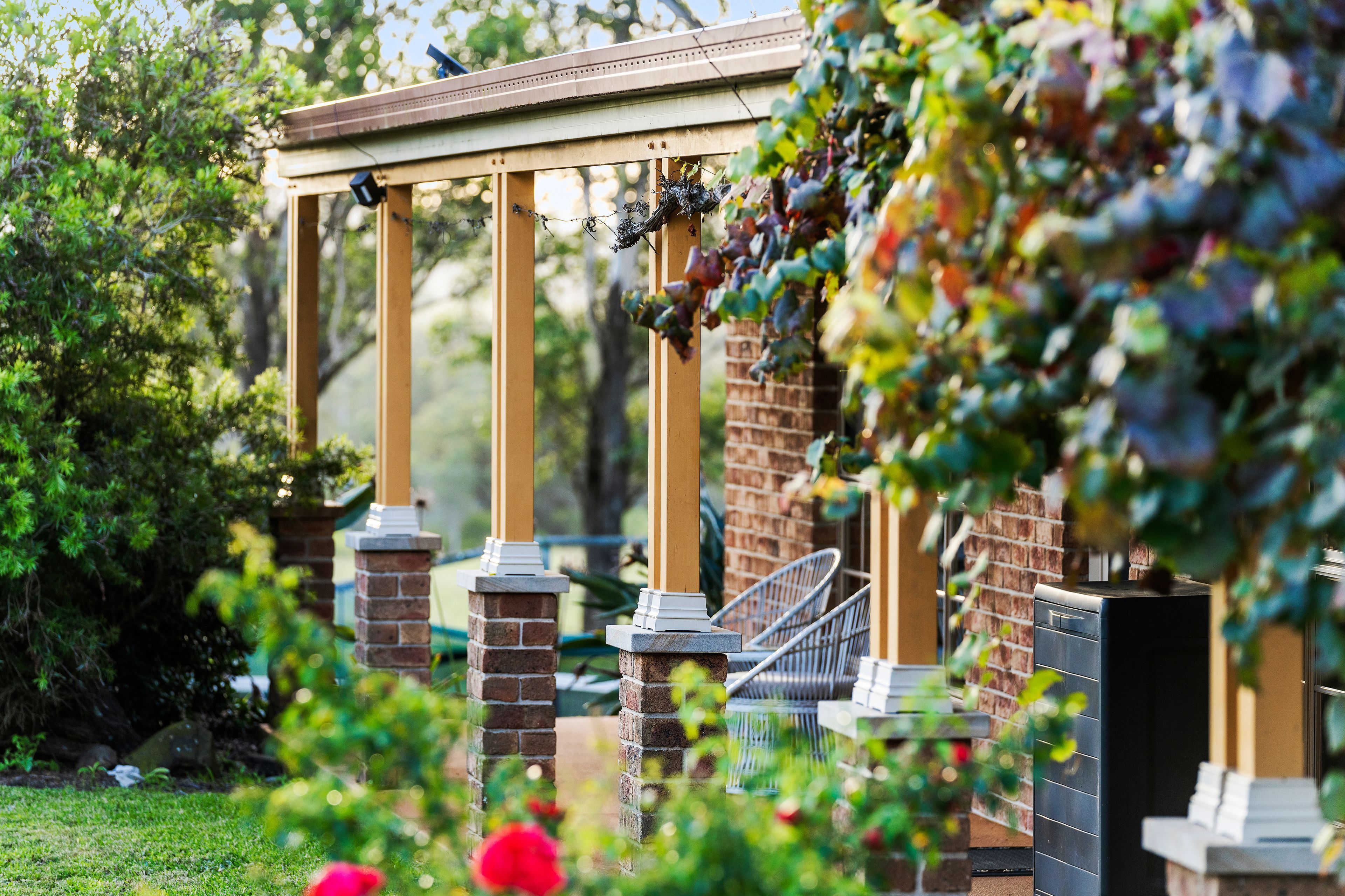 A garden with a pergola structure, brick pillars, and a seating area with metal chairs.