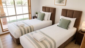 A hotel room with two beds, a window, a plant, and a lamp.
