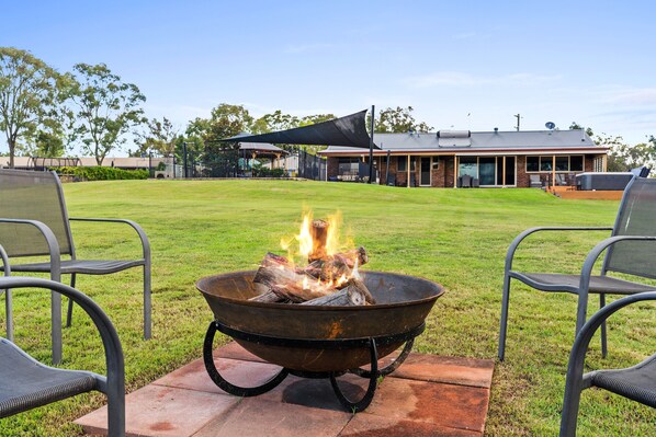 An outdoor seating area with a fire pit, chairs, and a building in the background.