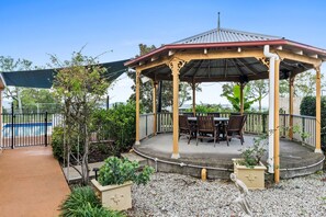 A gazebo with a table and chairs, surrounded by gravel and plants.