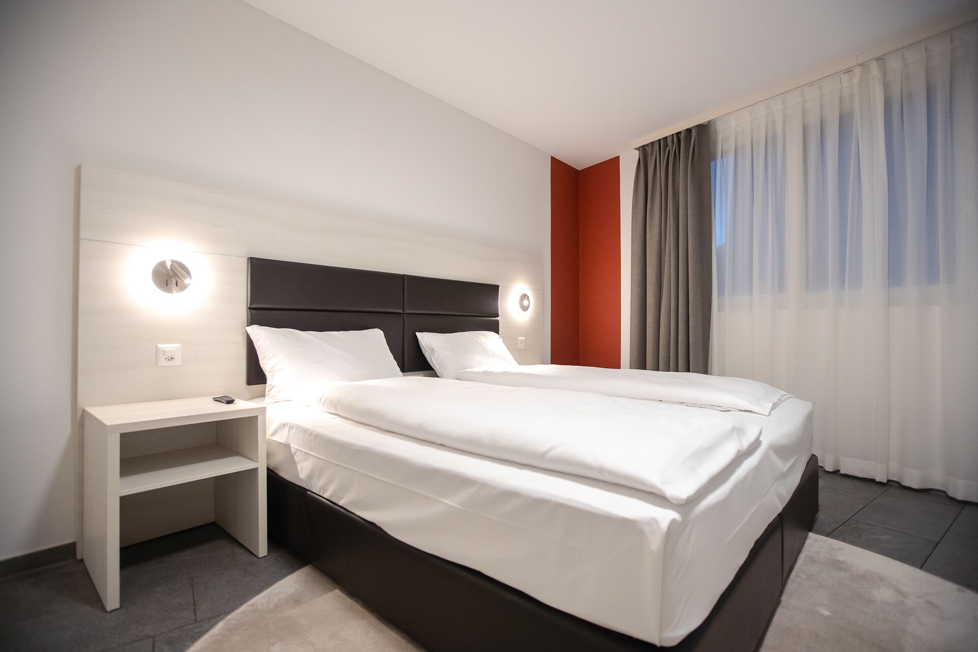A modern hotel room with a large bed, a bedside table, and a nightstand.