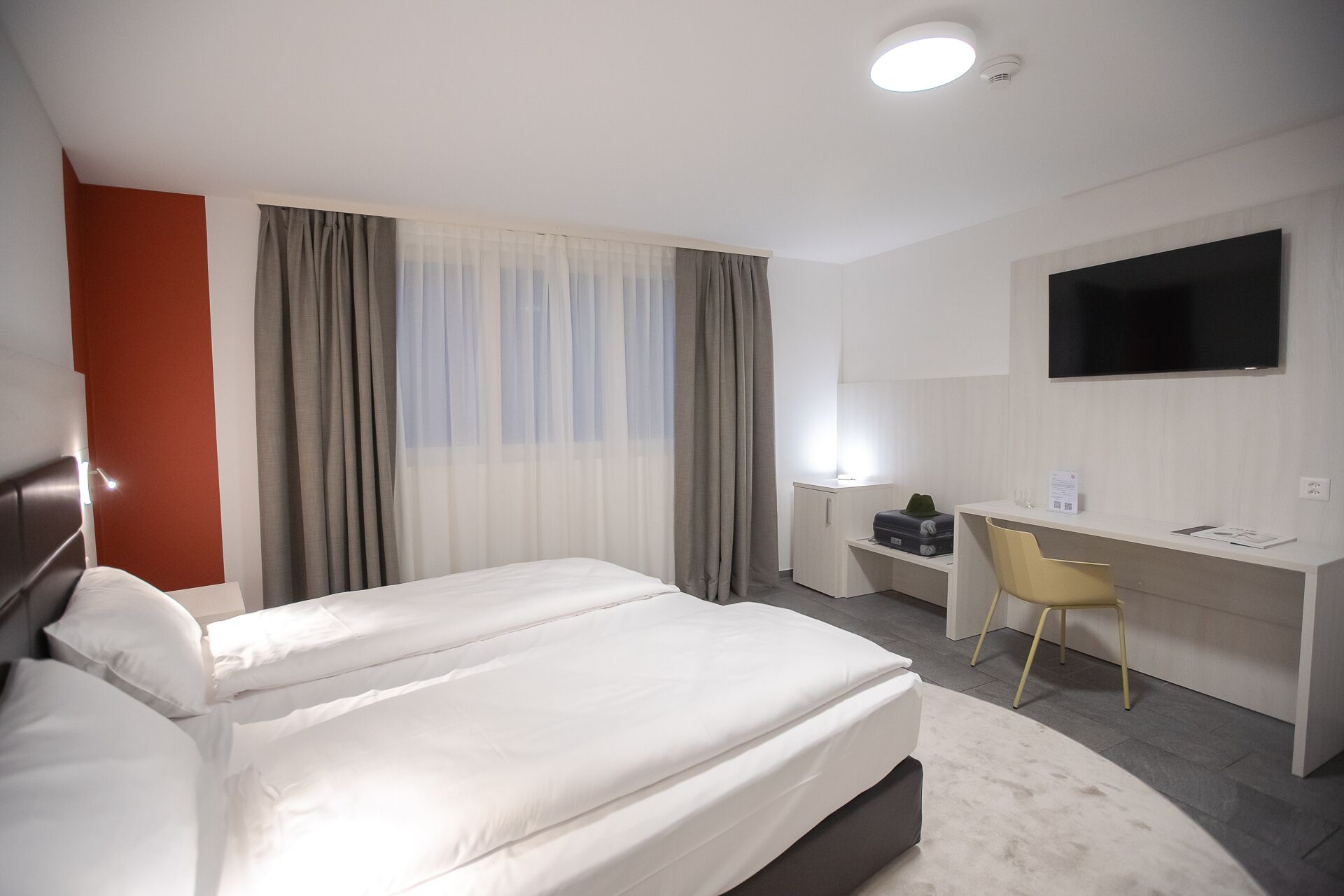 A hotel room with a bed, a desk, a chair, a TV, and a window with curtains.