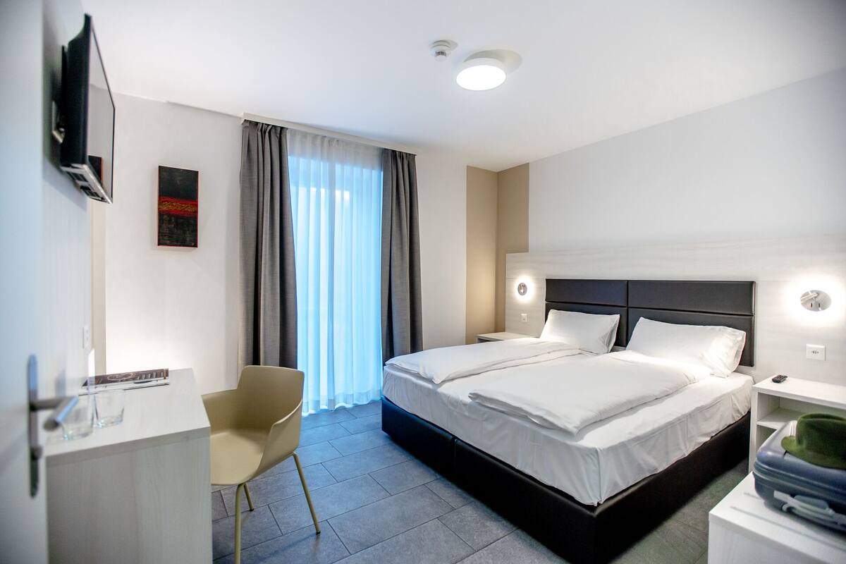 Ein modernes Hotelzimmer mit einem großen Bett, einem Schreibtisch, einem Sessel und einem Fernseher.