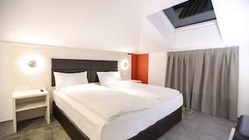 A hotel room with a large bed, a bedside table, a nightstand, a TV mounted on the wall, and a window with curtains.
