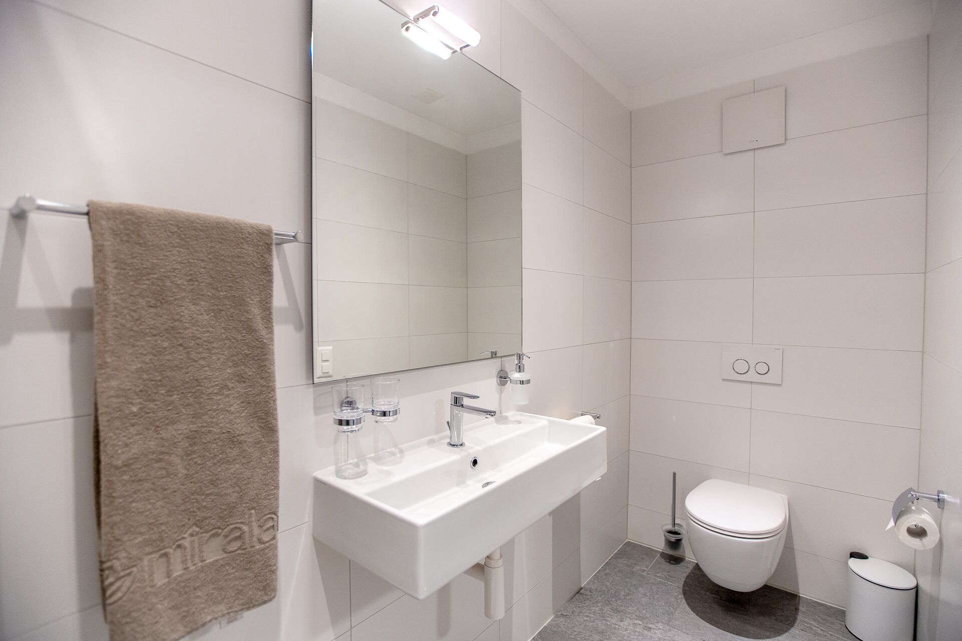 A modern bathroom with a white sink, mirror, and toilet.