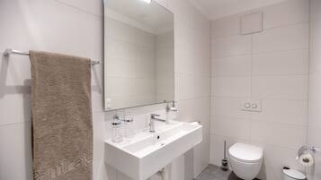 A modern bathroom with a white sink, mirror, and toilet.