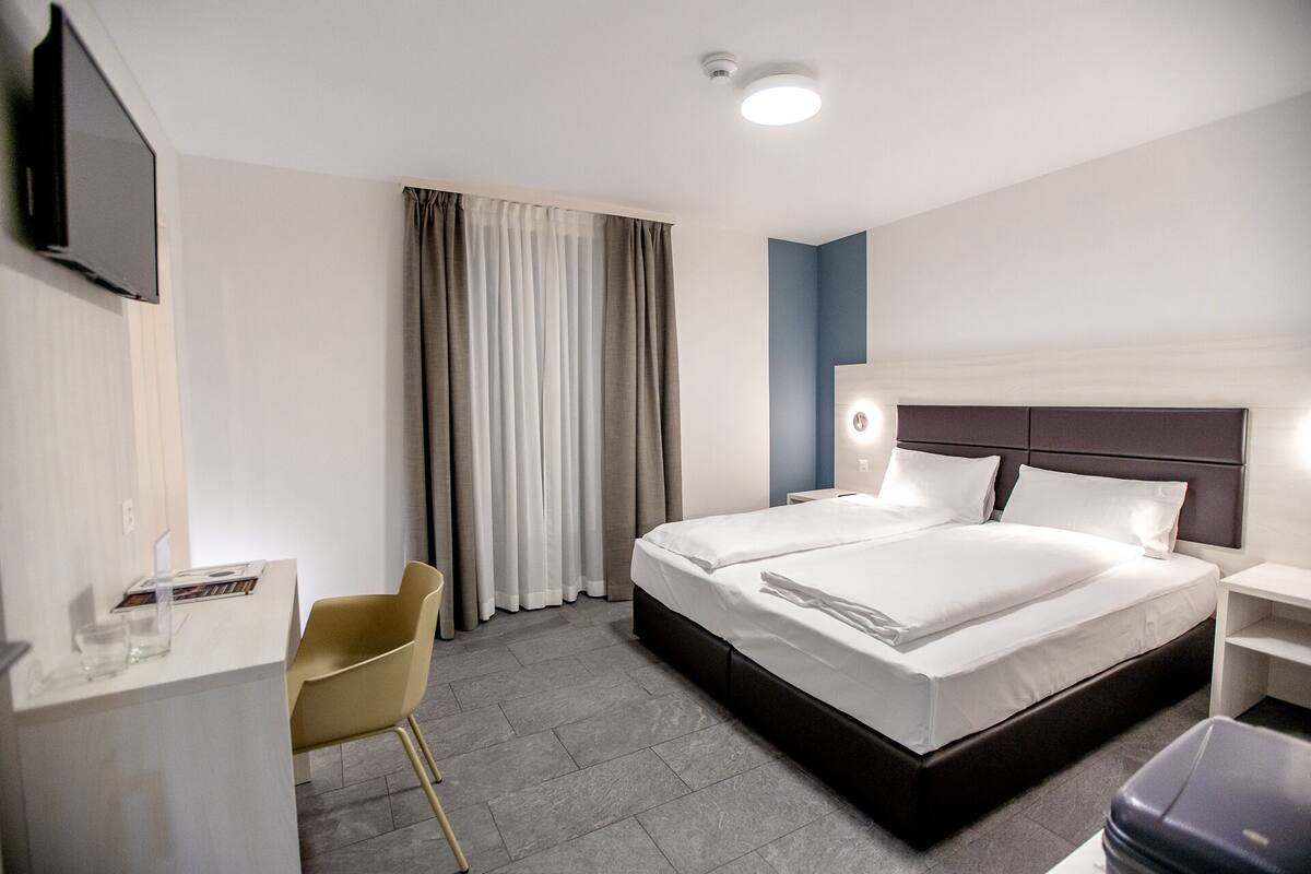 Ein Hotelzimmer mit einem großen Bett, einem Schreibtisch, einem Stuhl und einem an der Wand befestigten Fernseher.