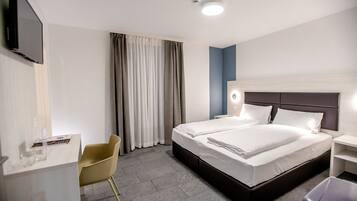 A hotel room with a large bed, a desk, a chair, and a TV mounted on the wall.