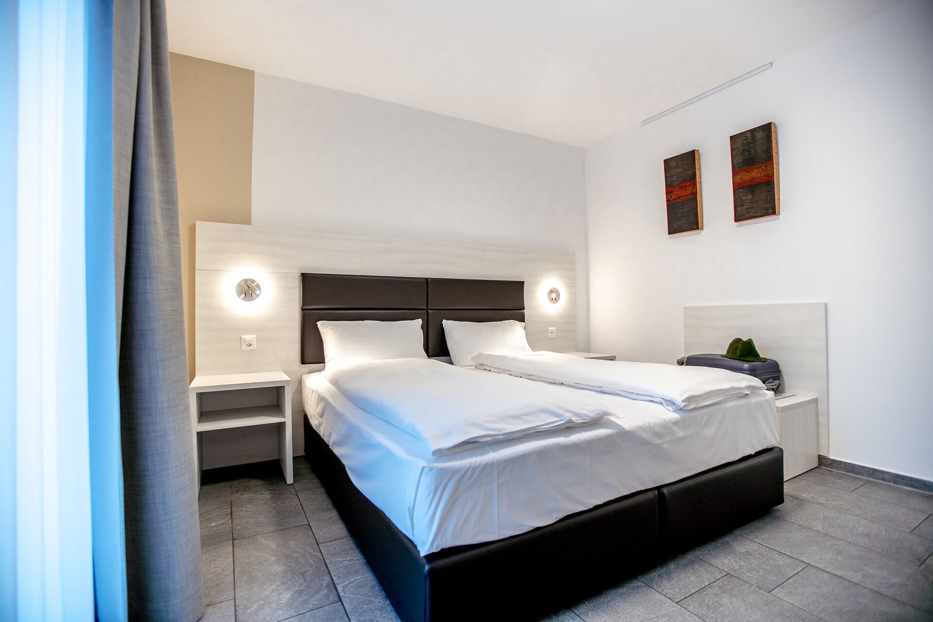 A modern hotel room with a double bed, two bedside tables, and a nightstand.