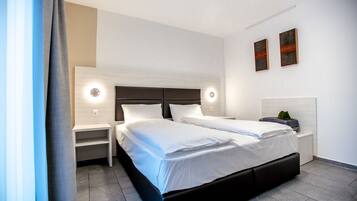 A modern hotel room with a double bed, two bedside tables, and a nightstand.