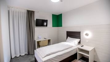 Ein Hotelzimmer mit Bett, Nachttisch, Schreibtisch mit Stuhl, einem an der Wand befestigten Fernseher und einer grünen Akzentwand.