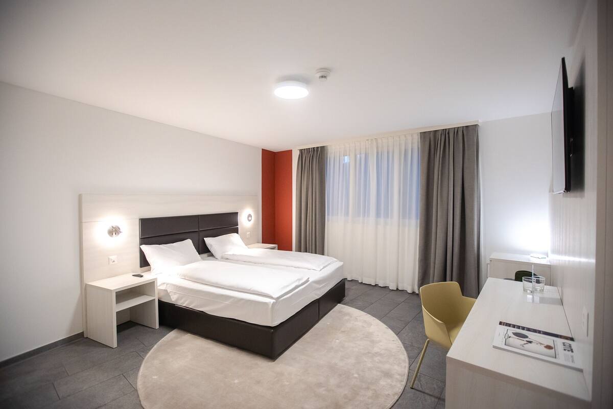Ein modernes Hotelzimmer mit einem großen Bett, Nachttischen, einem Schreibtisch und einem Sessel.