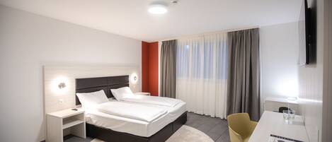Una habitación de hotel moderna con una cama grande, mesitas de noche, un escritorio y una silla.