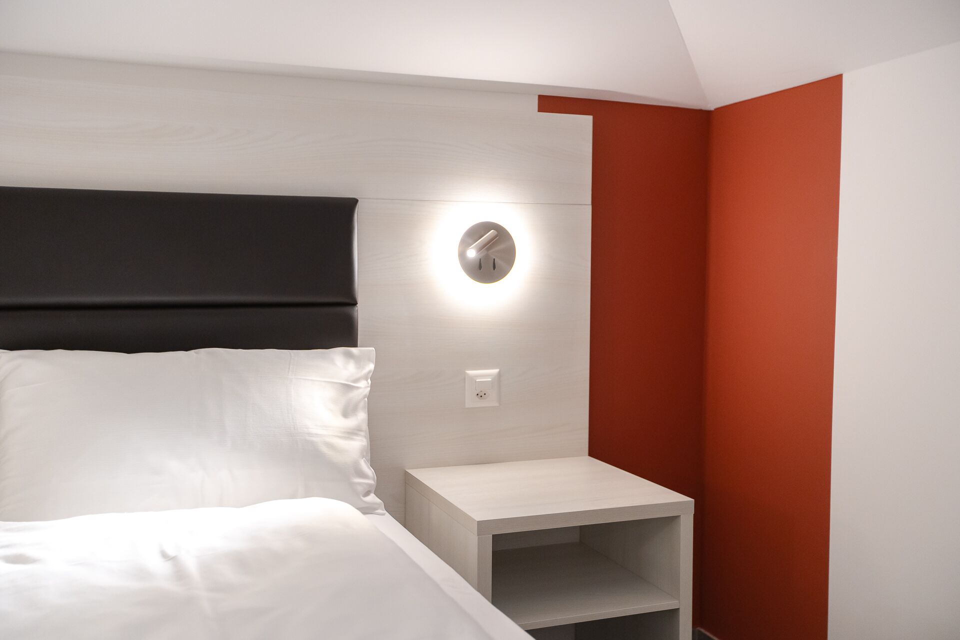 Een hotelkamer met een bed, een nachtkastje en een wandlamp.