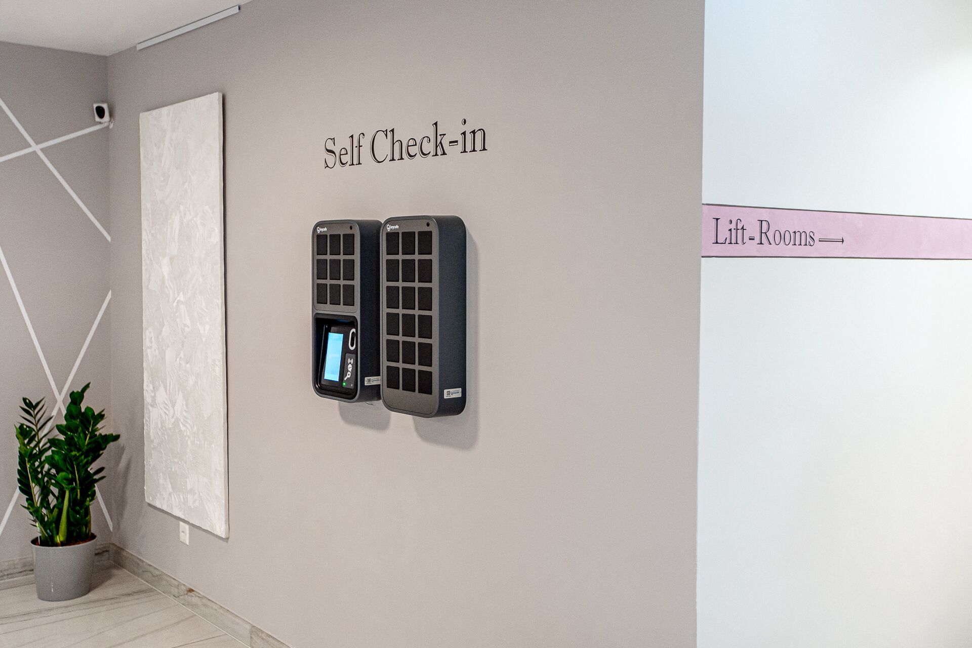 A self-check-in kiosk and a lift-room sign in a modern, minimalistic room.