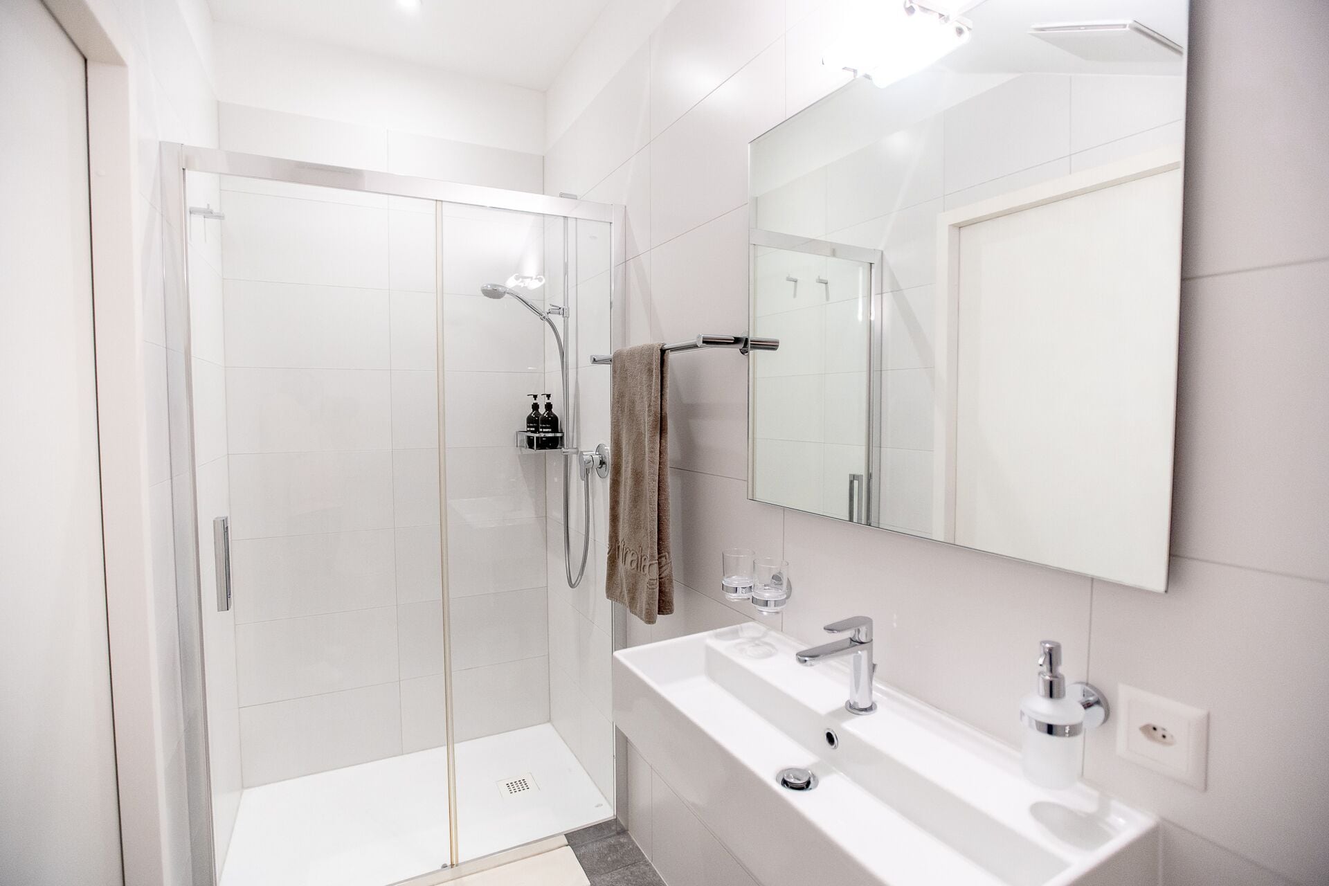 A modern bathroom with a glass-enclosed shower, a large mirror, and two sinks.