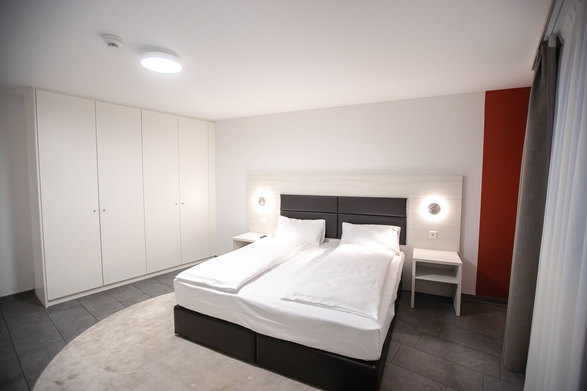 Un dormitorio moderno con una cama grande, un armario blanco y mesitas de noche.