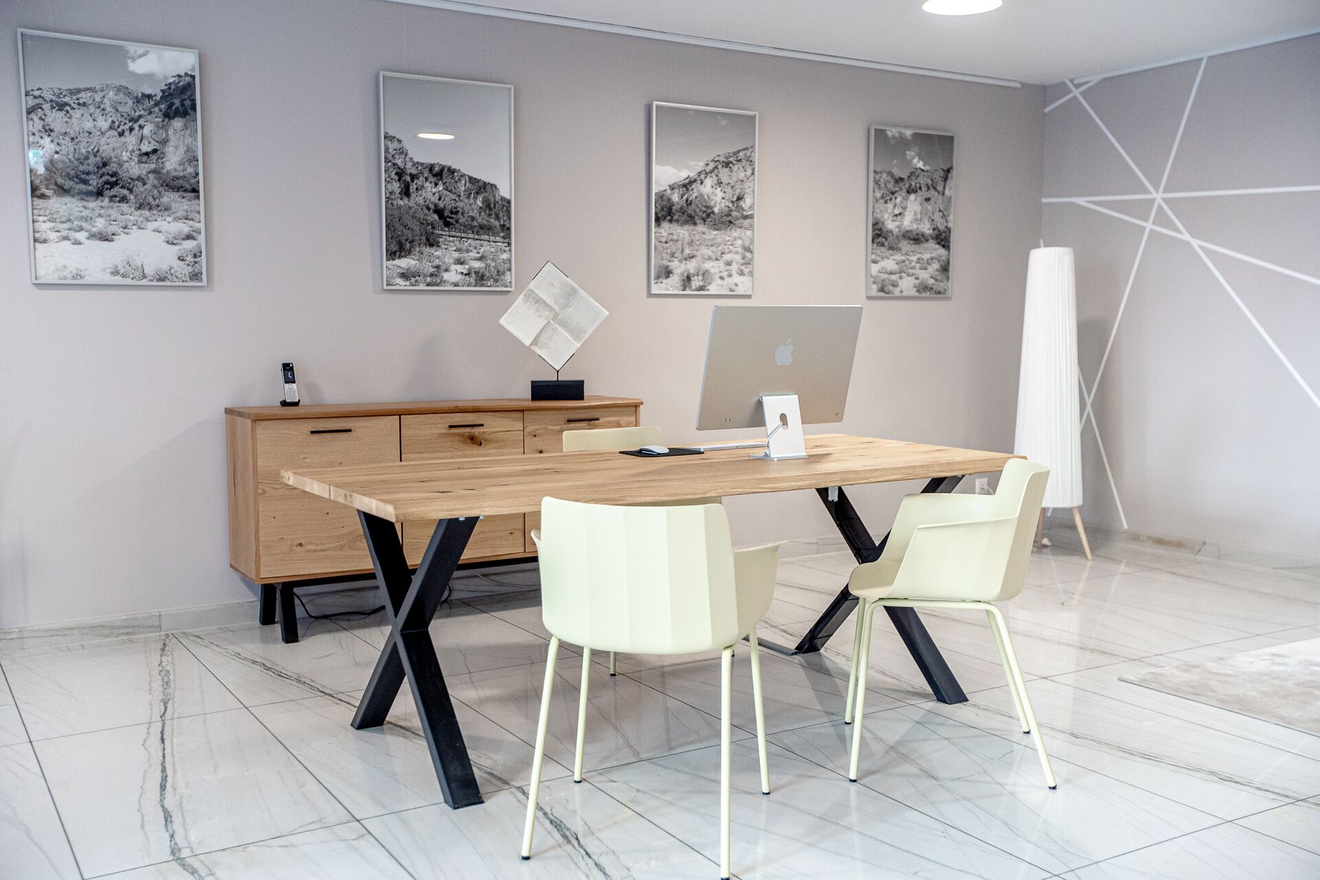 A modern office space with a wooden desk, two chairs, a computer, and framed pictures on the wall.