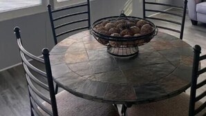 Un coin repas avec une table ronde et des chaises, un panier de pain, et une vue sur un lac grâce à de grandes fenêtres.