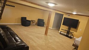 A living room with a large black leather couch, a flat-screen TV mounted on the wall, and a small table.