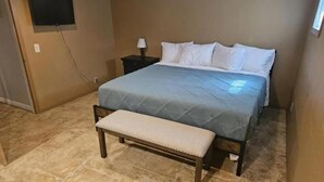 A bedroom with a bed, a bench, a nightstand, and a TV mounted on the wall.
