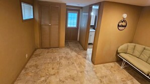 A hallway with a tiled floor, a closed wooden door, a window, and a couch.