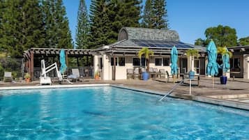 Une piscine entourée d’arbres, avec des chaises longues et des parasols, et un bâtiment doté d’un toit en pente.