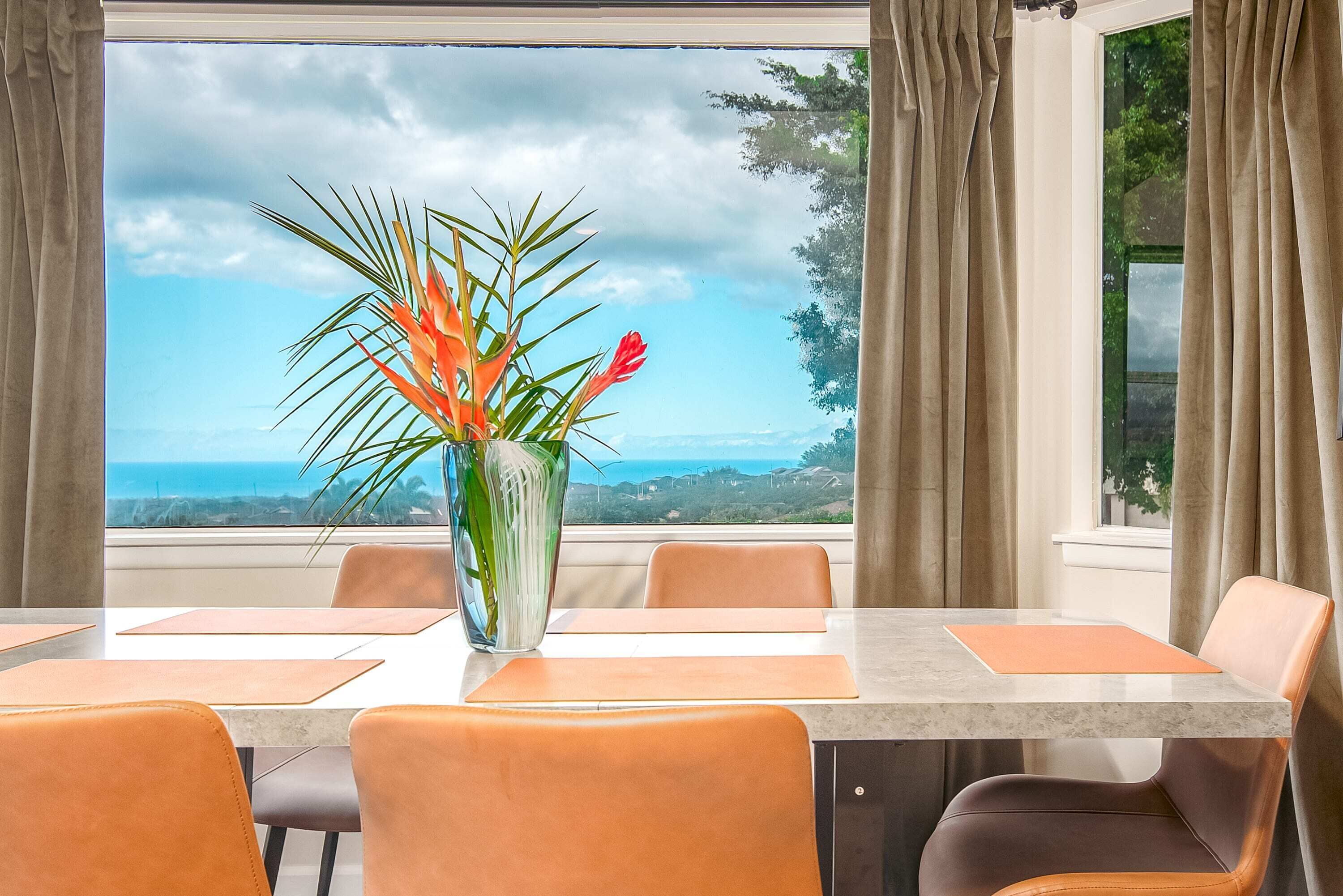 A dining area with a table and chairs, a vase with flowers, and a view of the ocean.