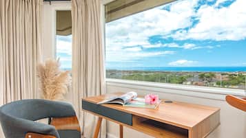A room with a wooden desk, a chair, and a view of the ocean.