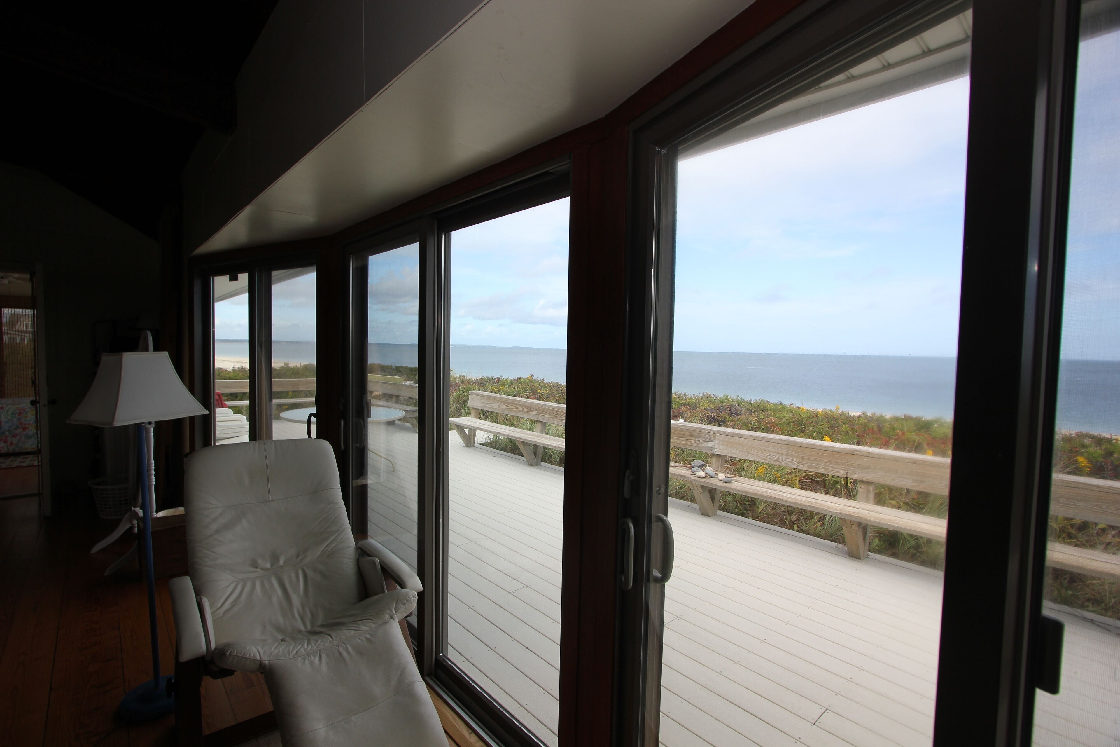 A room with a large window overlooking a wooden deck and the ocean.
