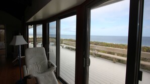 A room with a large window overlooking a wooden deck and the ocean. - 36 Salt Marsh Rd (Sandwich)