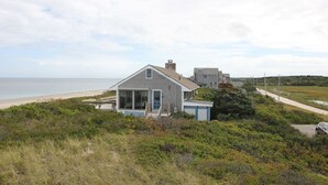 A coastal house with a large window, a small porch, and a view of the beach. - 36 Salt Marsh Rd (Sandwich)