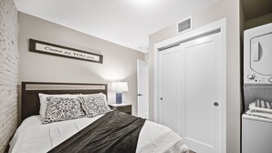 A bedroom with a bed, a nightstand with a lamp, a wardrobe, and a laundry machine. - Perfetto North End 1brm  (Boston)