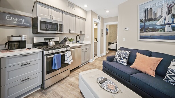A modern kitchen with stainless steel appliances, a blue and white patterned sofa, and a cityscape painting on the wall. - Perfetto North End 1brm  (Boston)