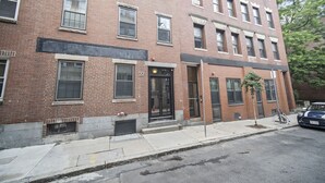 A multi-story brick building with a fire escape, a bicycle parked outside, and a car parked on the street. - Perfetto North End 1brm  (Boston)