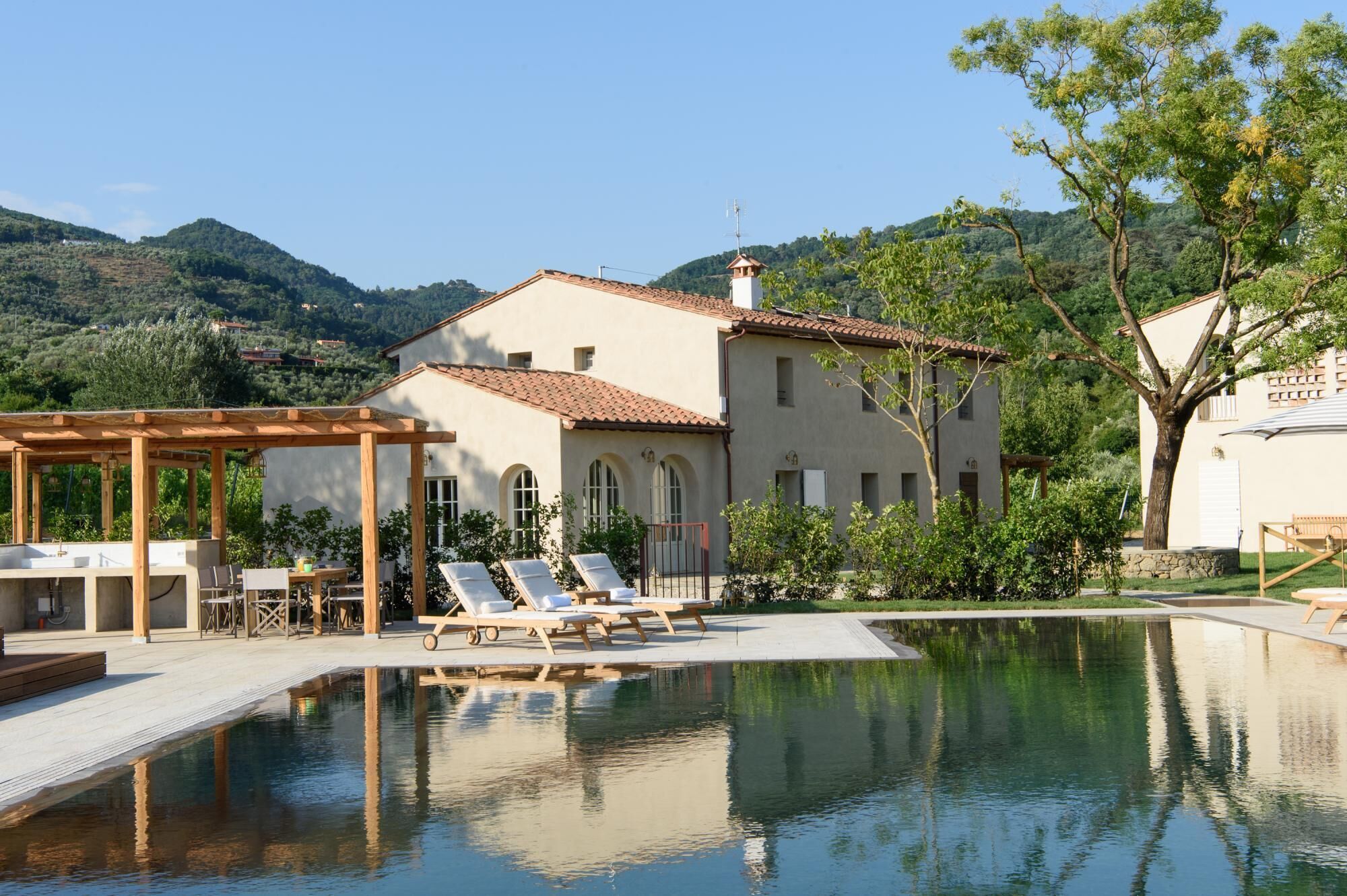A poolside area with lounge chairs, a pergola, and a building with a tiled roof.