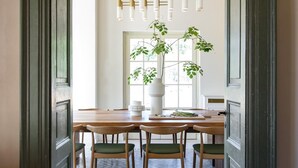 Een eethoek met een houten tafel, groene stoelen, een hanglamp en een bloempot met plant.