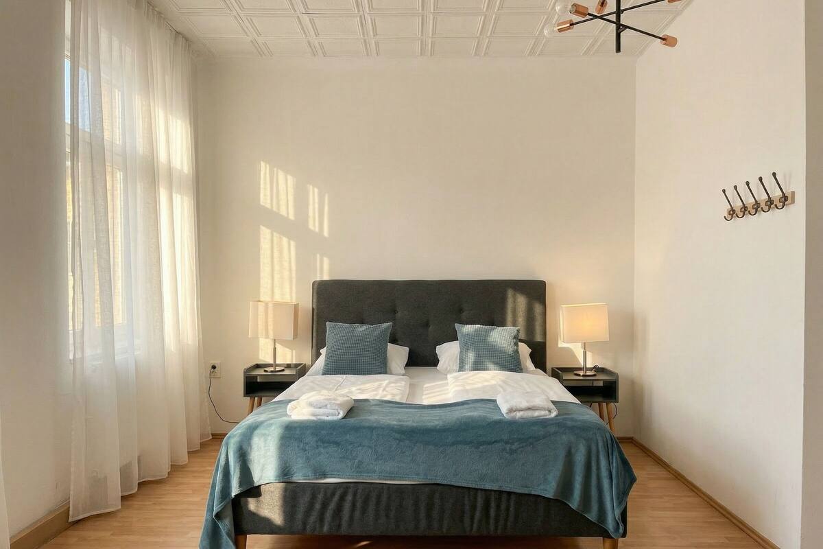 A hotel room with a bed, two bedside tables with lamps, a coat rack, and sheer curtains.