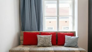 A wooden bench with red and grey cushions, positioned in front of a window with a view of buildings. - Big 3BR shared Apt. Perfect location (Vienna)