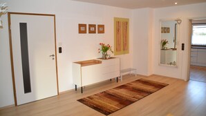 Um interior moderno com piso de madeira, um console branco com um vaso de flores e um espelho na parede.