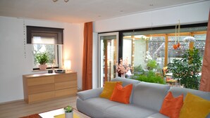 Uma sala de estar moderna com sofá cinza, almofadas laranja, mesa de centro de madeira e uma planta em vaso.